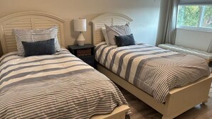 Une chambre à coucher avec deux lits, chacun doté de draps et d’oreillers à rayures, une table de chevet avec une lampe et une fenêtre avec des rideaux.