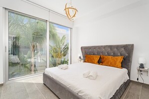 Ein modernes Schlafzimmer mit einem großen Bett, einer Glastür, die auf einen Balkon führt, und einer Pendelleuchte.