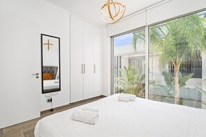 A modern hotel room with a large bed, a mirror, a wardrobe, and a view of a tropical garden.