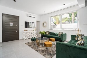 Un salon moderne avec un canapé vert, une table basse ronde et un téléviseur fixé au mur.
