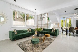 A modern living room with a green sofa, a glass coffee table, and a dining area with chairs and a table.