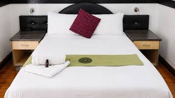 A neatly made bed with a white duvet, a single red pillow, and a green decorative strip. There are two bedside tables with lamps, one on each side of the bed.