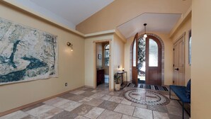 Un hall d’entrée spacieux avec un sol carrelé, une grande peinture abstraite, une porte en bois et un banc bleu.
