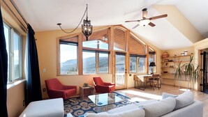 Un salon spacieux avec un grand canapé, deux fauteuils rouges, une table basse en verre et une vue sur les montagnes grâce à de grandes fenêtres.