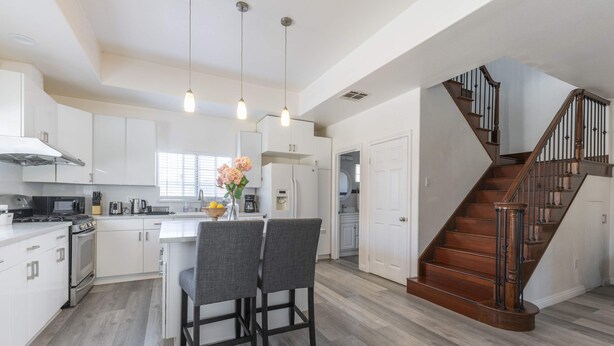 A modern kitchen with white cabinetry, a central island, and a wooden staircase. - Chic Cozy Home - Perfect Southern California Getaway (Rosemead)