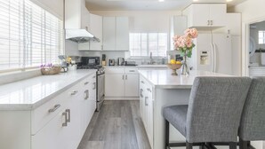 A modern kitchen with white cabinets, a central island, and pendant lighting. - Chic Cozy Home - Perfect Southern California Getaway (Rosemead)