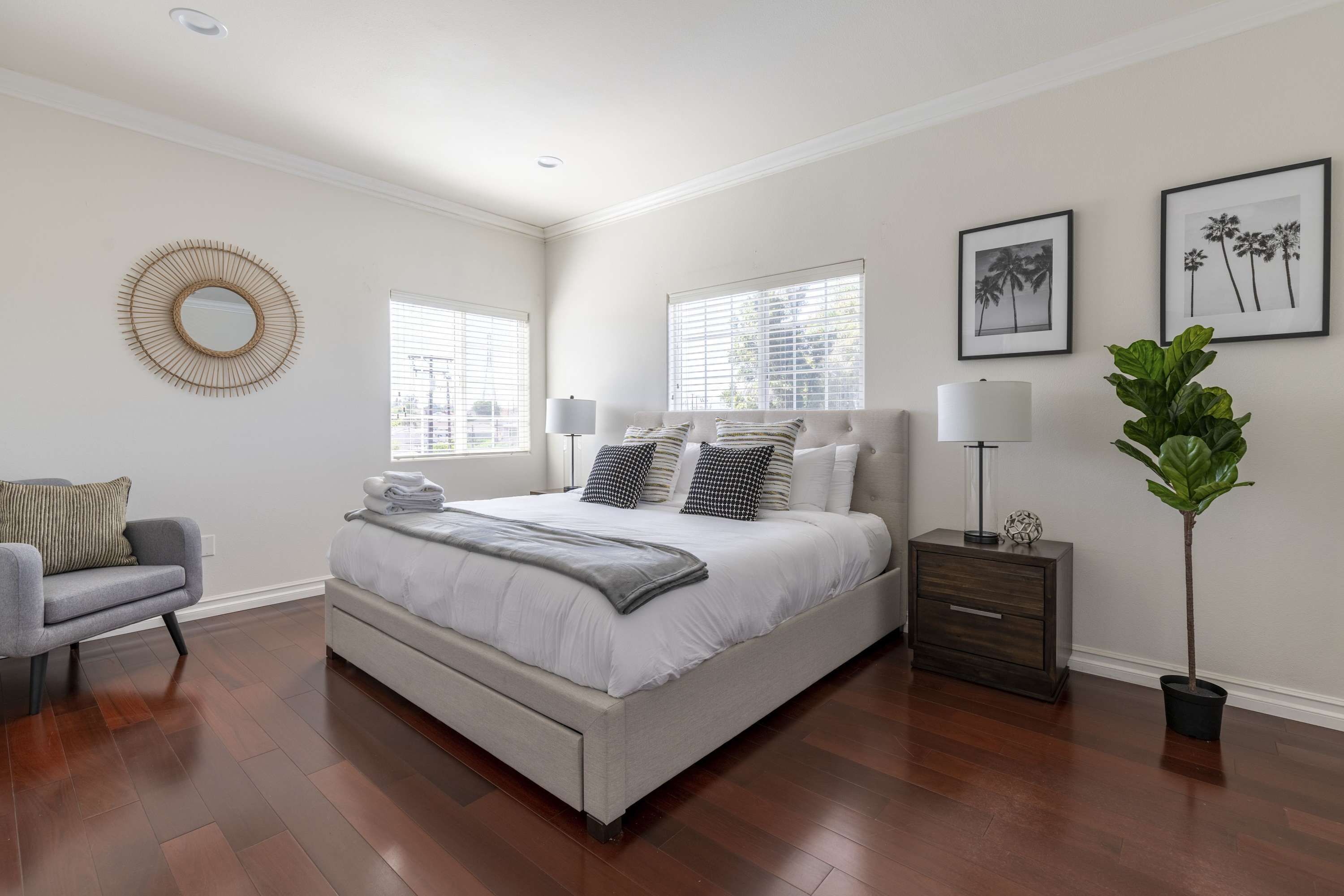 A bedroom with a large bed, a bedside table with a lamp, a chair, and a potted plant.