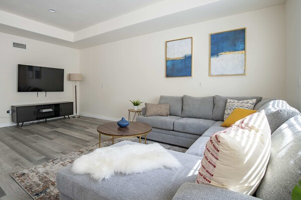 A modern living room with a grey sofa, a flat-screen TV, a coffee table, and two abstract paintings.