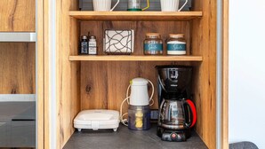 Una cocina con estantes de madera, una cafetera, una balanza y frascos sobre la encimera.