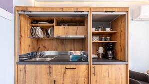Cocina compacta con armarios de madera, pileta de acero inoxidable y cafetera.