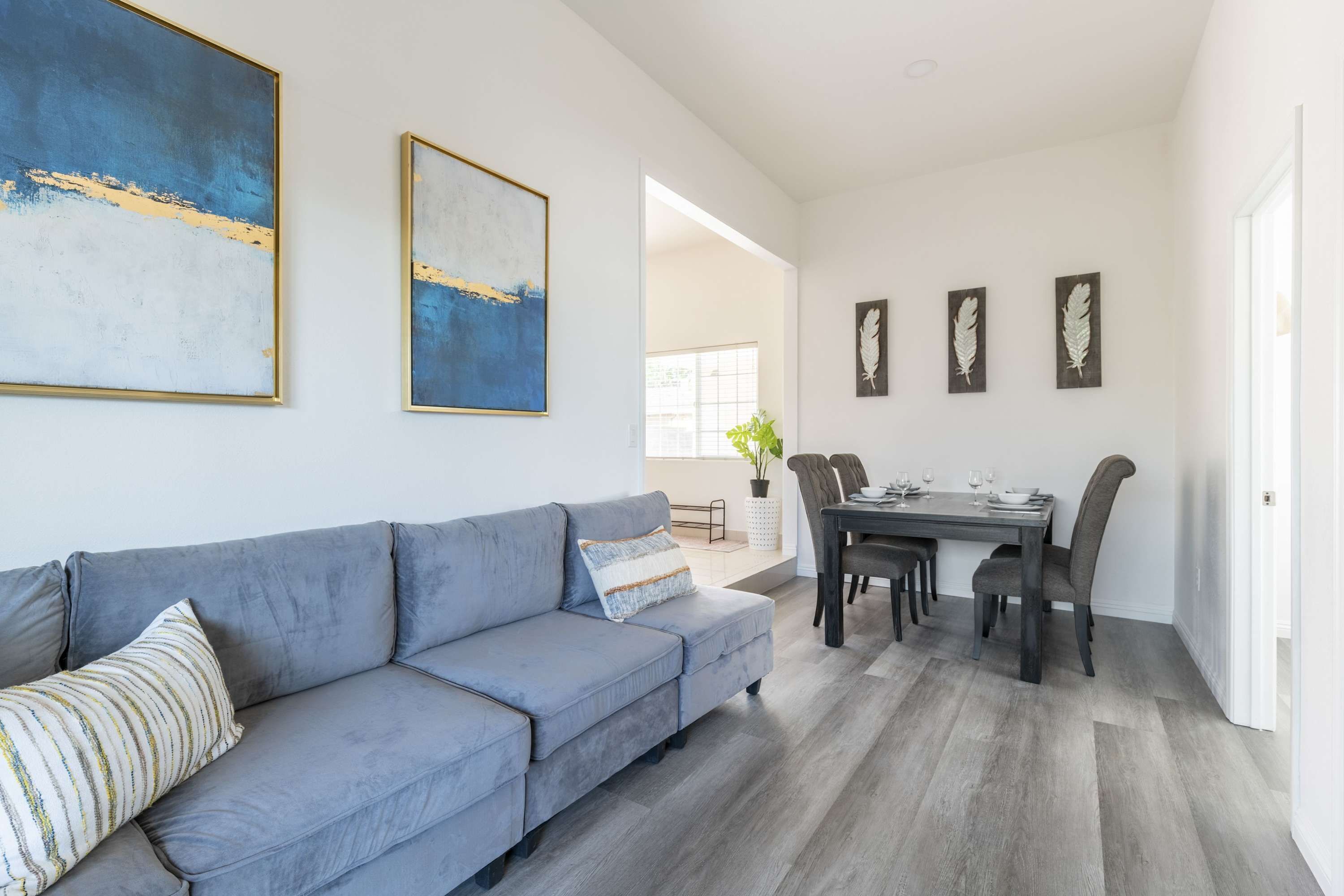 A modern living room with a grey sofa, a dining table with chairs, and abstract wall art.