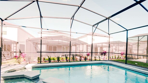 A swimming pool with a glass enclosure, surrounded by a garden with various plants and flowers. - 16239 7BR Stunning Home For Your Family Vacation (Clermont)