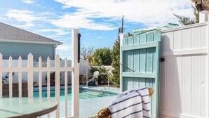 A pool area with a white fence, a lounge chair, and a table.