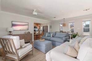 Un salon spacieux avec un grand canapé, un fauteuil en bois et un coin repas à l’arrière-plan.