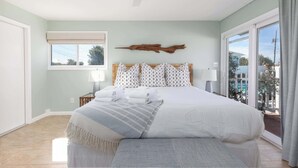 A spacious bedroom with a large bed, a ceiling fan, a window with a view, and a wooden wall decor.