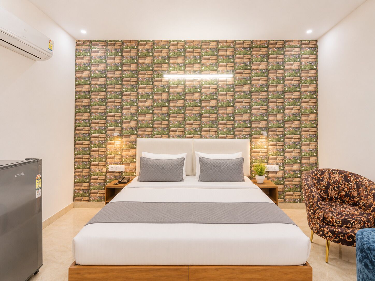 A bedroom with a bed, bedside tables, a refrigerator, and a patterned wall.