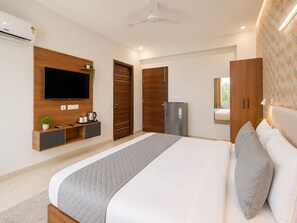 Ein modernes Schlafzimmer mit einem großen Bett, einem an der Wand montierten Fernseher, einem Kleiderschrank, einem Kühlschrank und einem Deckenventilator.