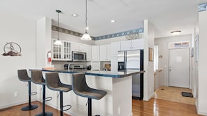 A modern kitchen with white cabinets, a central island with bar stools, stainless steel appliances, and pendant lighting.