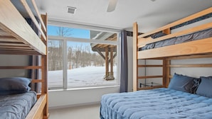 A room with bunk beds, a large window with a view of a snowy landscape, and a ceiling fan.