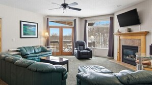 A living room with a sofa set, a fireplace, a television, and a balcony with a view.