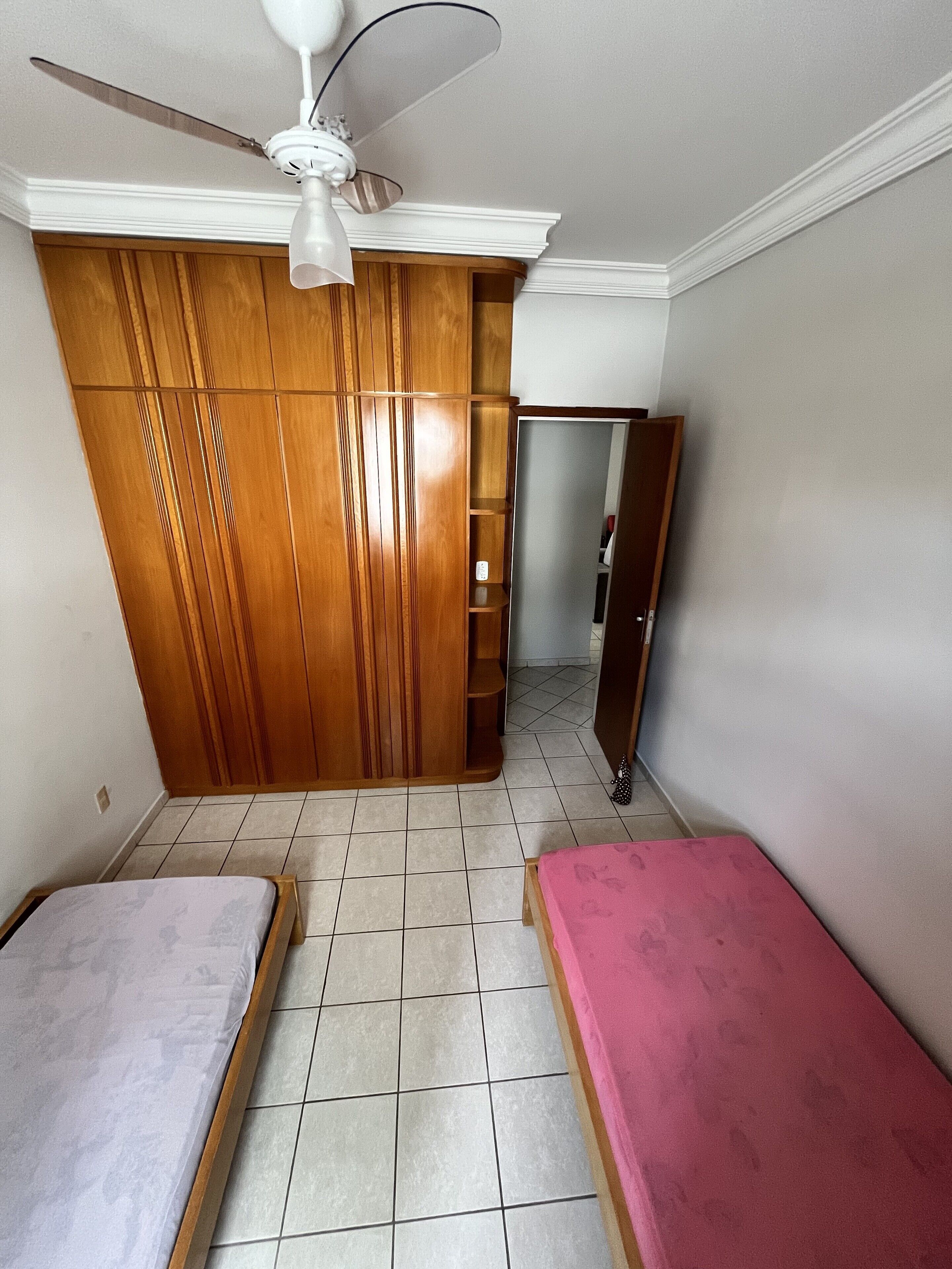 Un dormitorio con dos camas individuales, un armario de madera, ventilador de techo y suelo de baldosas.