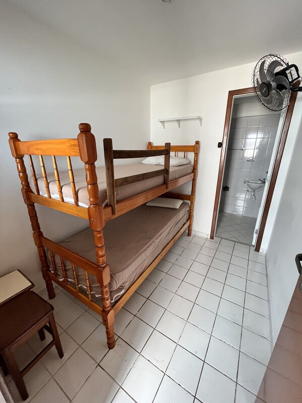 A bunk bed in a room with white tiled floors, a small wooden table, and a fan mounted on the wall. - Guarapari Praia Frente Mar (Guarapari)