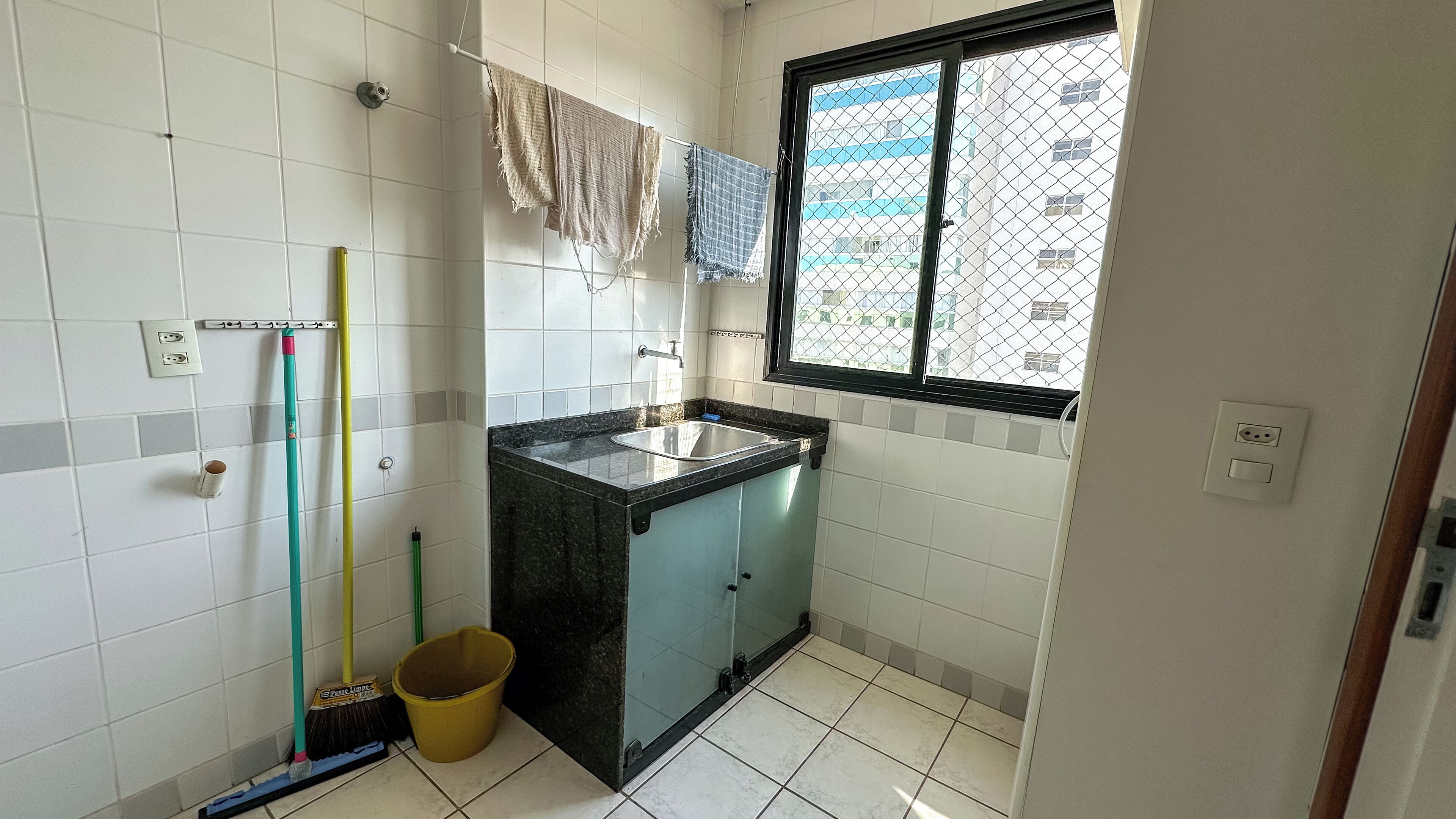 A small bathroom with a sink, a window, and a mop on the floor.