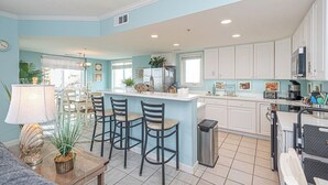 A kitchen with a central island, bar stools, and a dining area with chairs. - Jetty's Break-Beautiful 3 Bedroom Condo steps from the beach! (Ocean City)