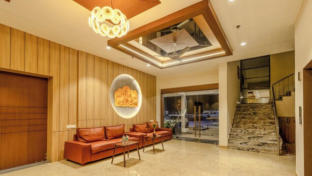 A modern lobby with a wooden wall, a circular light fixture, a sofa set, and a staircase. - Daksh The Grand Govardhan Dwarka (Dwarka)