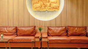 A room with a brown leather sofa, a small wooden table, and a decorative wall piece. - Daksh The Grand Govardhan Dwarka (Dwarka)
