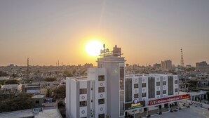 A building with a sign reading "Daksh The Grand Goverdhan" and a view of a cityscape with the sun setting in the background. - Daksh The Grand Govardhan Dwarka (Dwarka)
