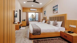 A modern hotel room with a large bed, wooden headboard, bedside tables, a desk, and a ceiling fan. - Daksh The Grand Govardhan Dwarka (Dwarka)