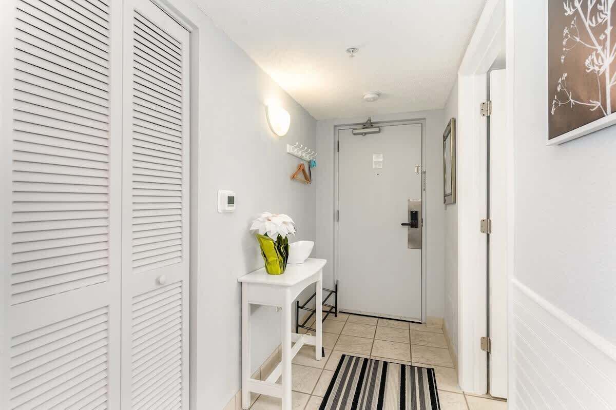 A hallway with white walls, a white door, a white table with a vase of flowers, and a striped rug.