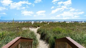 A beach path leading to the ocean with beach umbrellas and people in the distance. - Luxury Beachfront Resort Condo (Myrtle Beach)