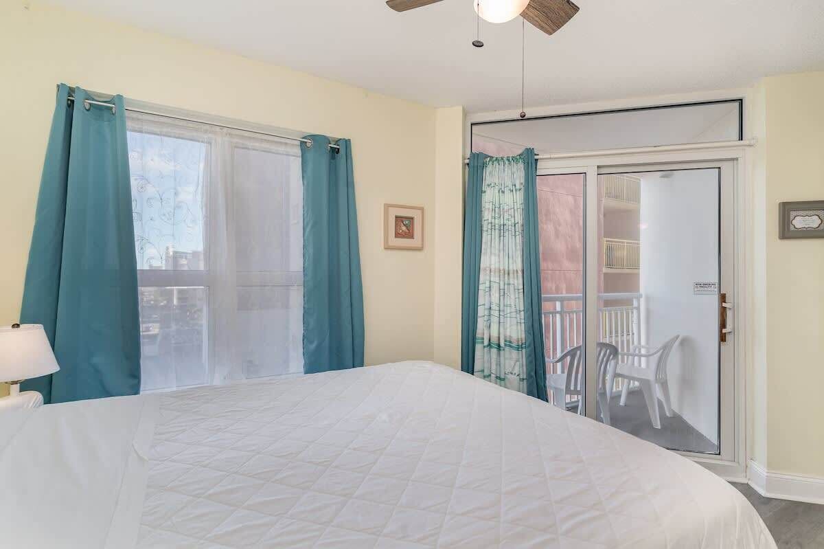 A bedroom with a bed, a ceiling fan, and a sliding glass door leading to a balcony.