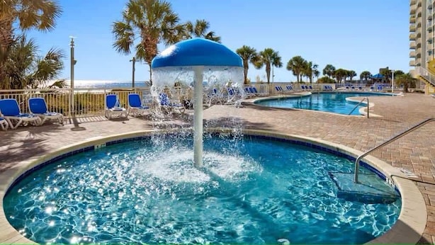 A pool area with a water fountain, lounge chairs, and palm trees. - Luxury Beachfront Resort Condo (Myrtle Beach)