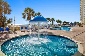 A pool area with a water fountain, lounge chairs, and palm trees.