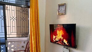 Ein Wohnzimmer mit Fernseher, der einen Kamin zeigt, einem Sofa, einem kleinen Tisch und einem Sessel.