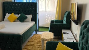 Ein Hotelzimmer mit einem Bett, zwei grünen Sofas, einem kleinen Tisch, einem Fernseher und einem Fenster mit Vorhängen.