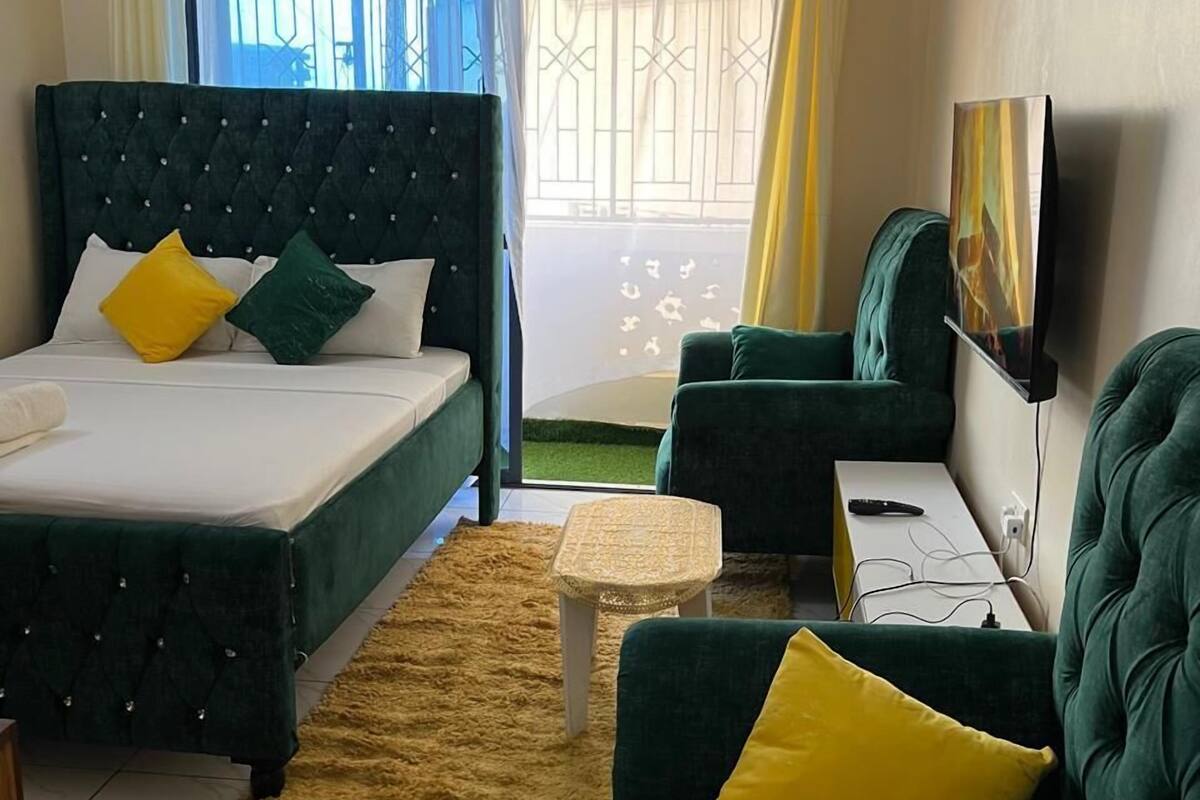 Une chambre d’hôtel avec un lit, deux canapés verts, une petite table, un téléviseur et une fenêtre avec des rideaux.