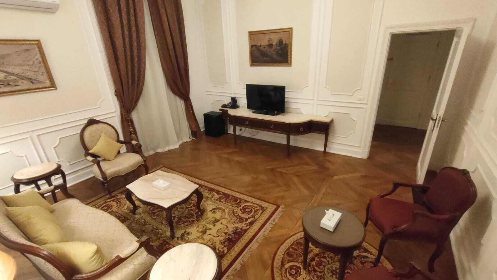 A living room with a sofa, armchairs, a coffee table, a TV, and a patterned rug.