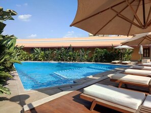 A swimming pool with lounge chairs and umbrellas, surrounded by tropical plants. - Maison Maxim De Lesseps (Ismailia)