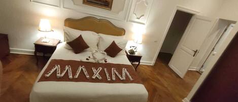 A hotel room with a bed, two bedside tables, a nightstand, a door, and a wall with a framed picture.