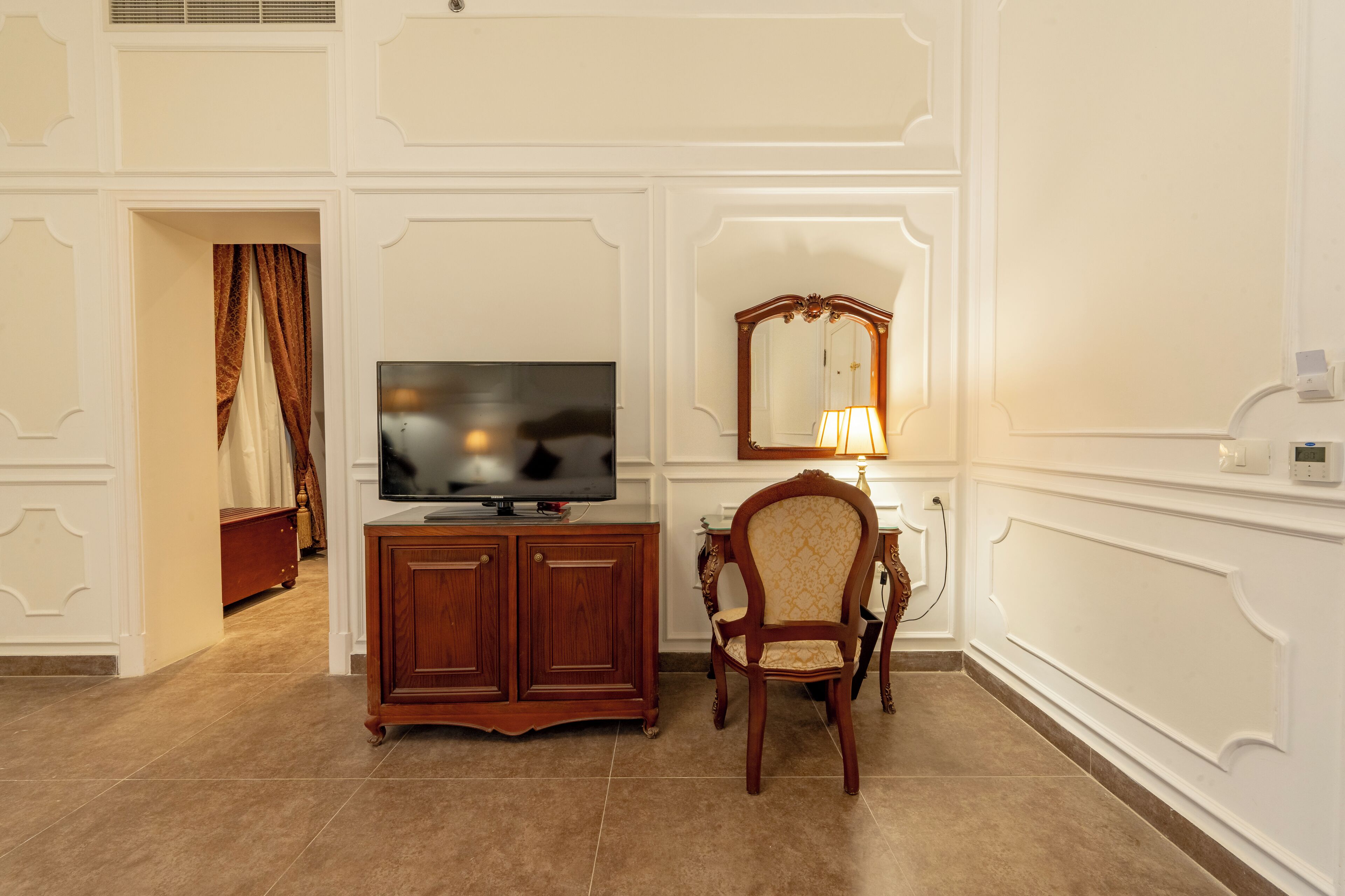 Ein Hotelzimmer mit Holzschrank, Fernseher, Sessel und Spiegel.
