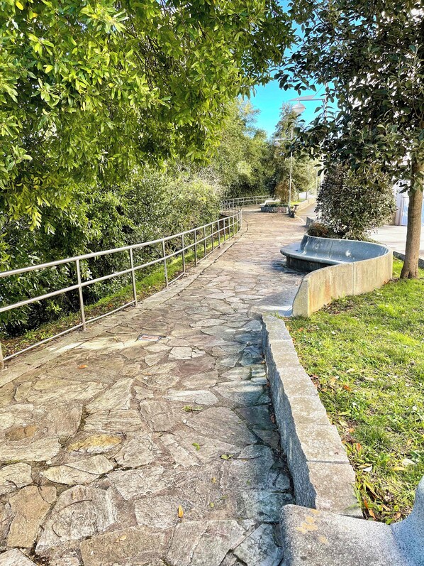 Un sendero de piedra con barandillas metálicas, rodeado de exuberante vegetación y un cielo azul despejado.