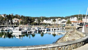 A marina with boats docked, a stone wall, and buildings in the background. - The Cliffs - Galician Blue Views (Ortigueira)