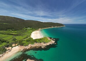 A coastal landscape with a sandy beach, lush greenery, and clear turquoise waters. - The Cliffs - Galician Blue Views (Ortigueira)