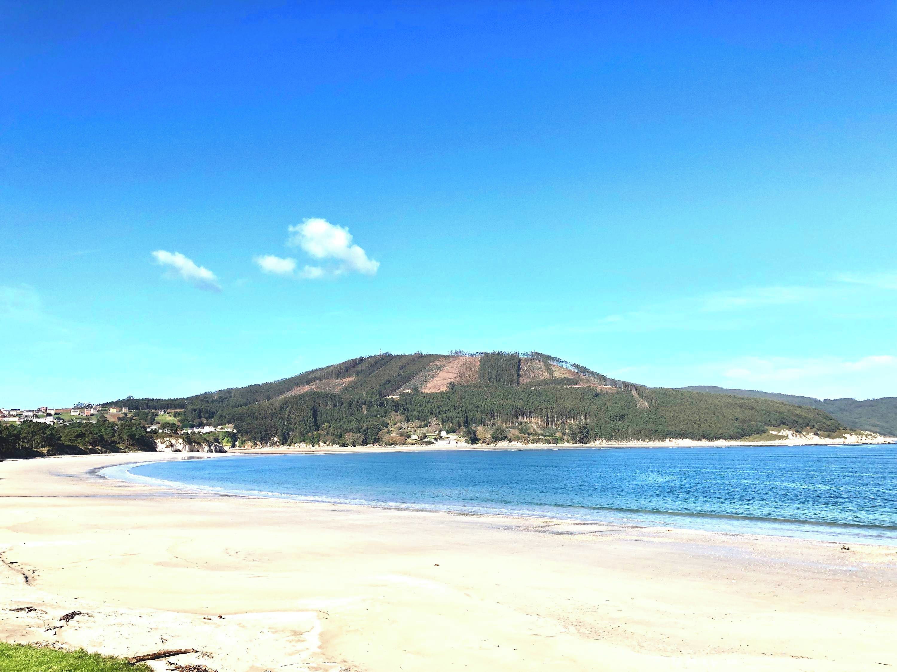 A beach with a mountain in the background, clear skies, and calm waters.