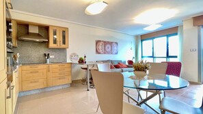 A modern kitchen with wooden cabinets and a dining area with a glass table and chairs. - The Cliffs - Galician Blue Views (Ortigueira)