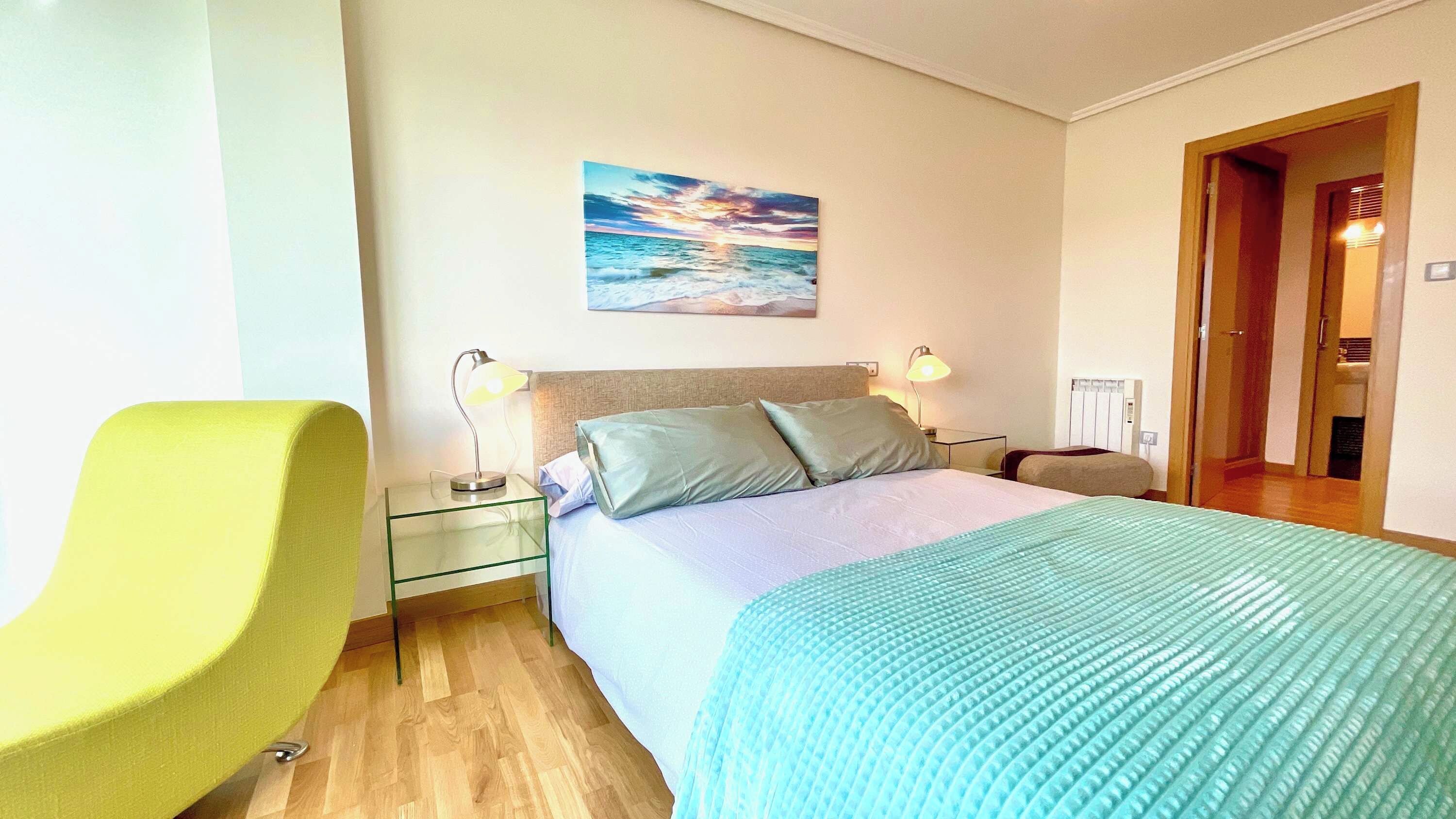 A hotel room with a bed, two bedside lamps, a nightstand, a chair, and a painting on the wall.